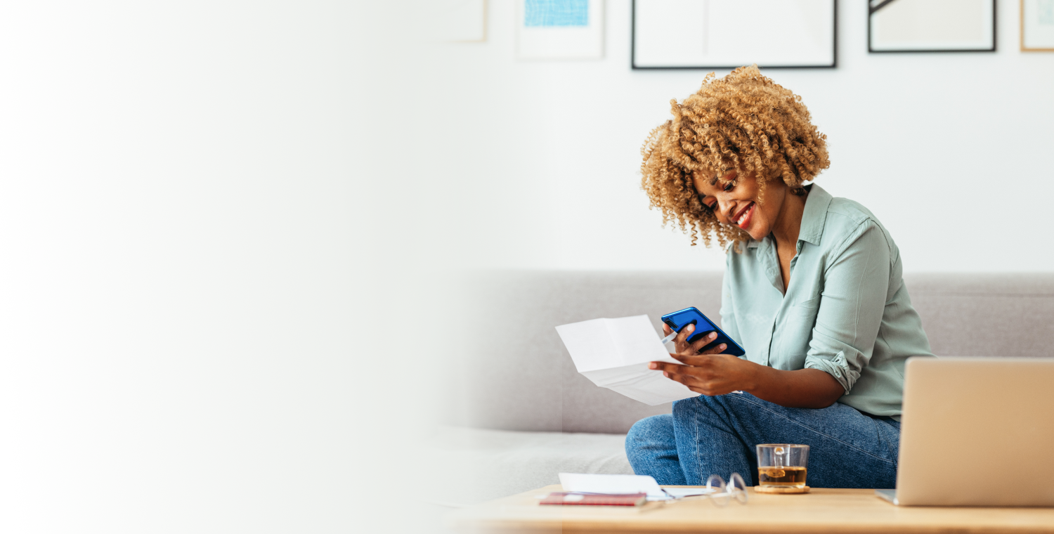 Person sitting on a couch holding a mobile phone and a bill